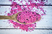 Pinkfarbener ungekochter Bio-Basmatireis auf Holzlöffel (Aufsicht)