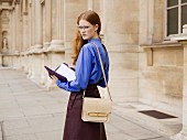 A young woman wearing a long-sleeved blouse and a leather skirt holding a document folder