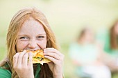 A red haired teenager biting into a sandwich