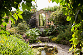 Gartenplatz mit Natursteinbelag und rundes Wasserbecken in blühendem Garten