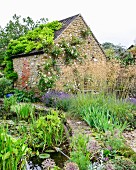 Garten mit Gartenteich vor rustikalem Haus aus Naturstein
