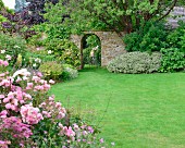 Clipped lawn, flowering shrubs and wrought iron gate in garden wall