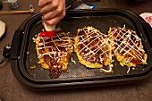 Okonomiyaki (Japanese pancakes) on a hot tray being decorated with mayonnaise