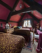 Schlafzimmer in bordeauxrot unter dunklem Holz-Dachstuhl, Betten mit elegantem Überwurf