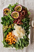 A large salad with green vegetables, marinated onions, passion fruit and Parmesan cheese