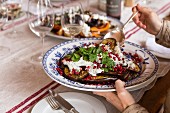 A woman serving oven roasted aubergines with Greek yoghurt and pomegranate seeds