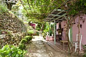 Mediterrane Terrasse mit begrünter Pergola und rosafarbener Fassade