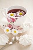 Tee mit Gänseblümchen in einer Tasse mit Blumenmuster
