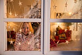 Girl looking out of window decorated with artificial snow and fairy lights
