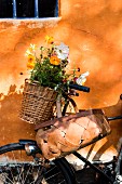 Basket of summer flowers on vintage bicycle leaning against orange façade with blue lattice window
