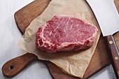 Raw lean entrecôte on a piece of paper on a chopping board (seen from above)