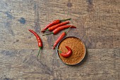 Chilli powder and fresh chillis on a wooden surface (seen from above)