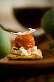 Cracker topped with cream cheese, bacon, a cherry tomato and Parmesan cheese