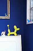 Gelbe Luftballon-Hundefigur vor blauer Wand