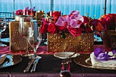 Table festively set with place settings and flower arrangements in gilt containers for Indian wedding