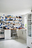 Shelves on blue and white wall tiles above kitchen counter on white base units in corner of kitchen