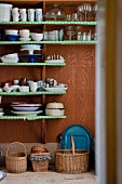 Crockery on shelves covered in green paper above various baskets on floor