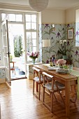 Esszimmer mit floraler pastellfarbener Tapete und massivem Esstisch, Blick in Wintergarten mit nostalgischem Flair