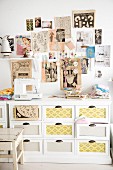 Wall decorated with clipping from retro fashion magazines above sewing utensils and sewing machine on top of white chest of drawers