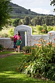 Frau und Kind vor Gartenmauer mit geöffneter Tür in sommerlichem Garten vor Hügellandschaft