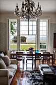 Sofa and coffee table in front of dining area in elegant interior with view of landscape through French windows