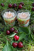 Tealight holders with patterns of cherries among cherries on grass