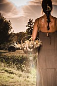 Frau in langem Sommerkleid mit Blütenkorb auf Wiese