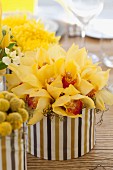 Bright table centrepiece; bouquets of yellow flowers in containers covered with striped fabric