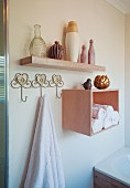 Towel hanging from hook next to rolled towels in shelf module below collection of vases on floating shelf
