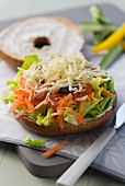 A bagel with a raw carrots salad and raisins