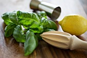 Ingredients for Gin Basil Smash: lemons, basil, a measuring cup and a wooden lemon juicer