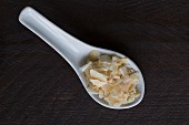 Coconut chips on a porcelain spoon on a dark wooden surface