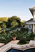 Geometrisch angelegter eleganter Landhaus-Garten mit weißen Blüten und Gartenbrunnen