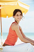 Junge Frau in Tanktop und Sommerhose sitzt auf Strandliege