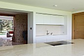 Narrow white fitted kitchen and open doorway leading into living room with stone chimney breast