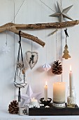 Christmas decorations hanging from rustic branch above lit candles in candlesticks