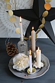 Christmas decorations and Advent wreath; four lit candles in various holders around paper flower in front of garland of gold paper discs