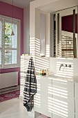 Licht- und Schattenspiel auf Waschtisch mit weißem Unterschrank und Wandarmatur unter Spiegel in Nische