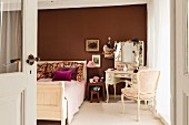 Antique-style double bed and dressing table against brown-painted wall