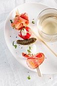 An antipasti skewer and white wine on white plate