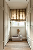 Roman blind on window in narrow dressing room with white, country-house-style wardrobes