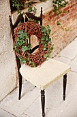 Wreath of wicker and ivy on chair against brick wall