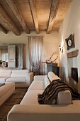 Elegante, weiße Sofagarnitur in Wohnzimmer mit Holzbalkendecke