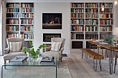 Dining area with rustic wooden furniture on delicate wire frames and armchairs in front of fireplace flanked by bookcases