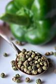 Dried green peppercorns on a spoon with a pepper in the background