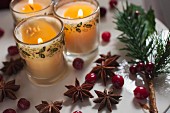 Three candles in glasses decorated for Christmas with bilberries and star anise