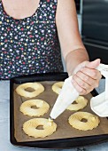 A woman piping choux pastry rings on a baking tray