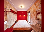 Bed against bright red wall and designer wallpaper on facing walls in narrow bedroom