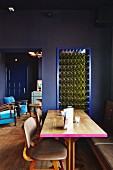 Wooden table with edge painted pink and leather-covered chairs in restaurant with dark blue walls