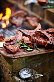 Grilled lamb chops on a wooden board next to a barbecue